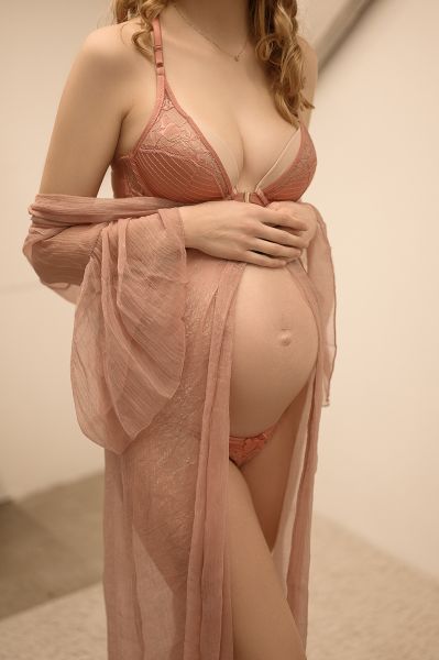 Sinnliches Babybauchfoto einer jungen Frau in rosa Dessous