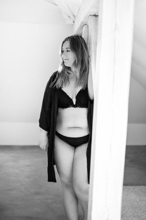 Sinnliches Schwarzweißfoto im Boudoir Stil von einer kurvigen jungen Frau in schwarzen Dessous